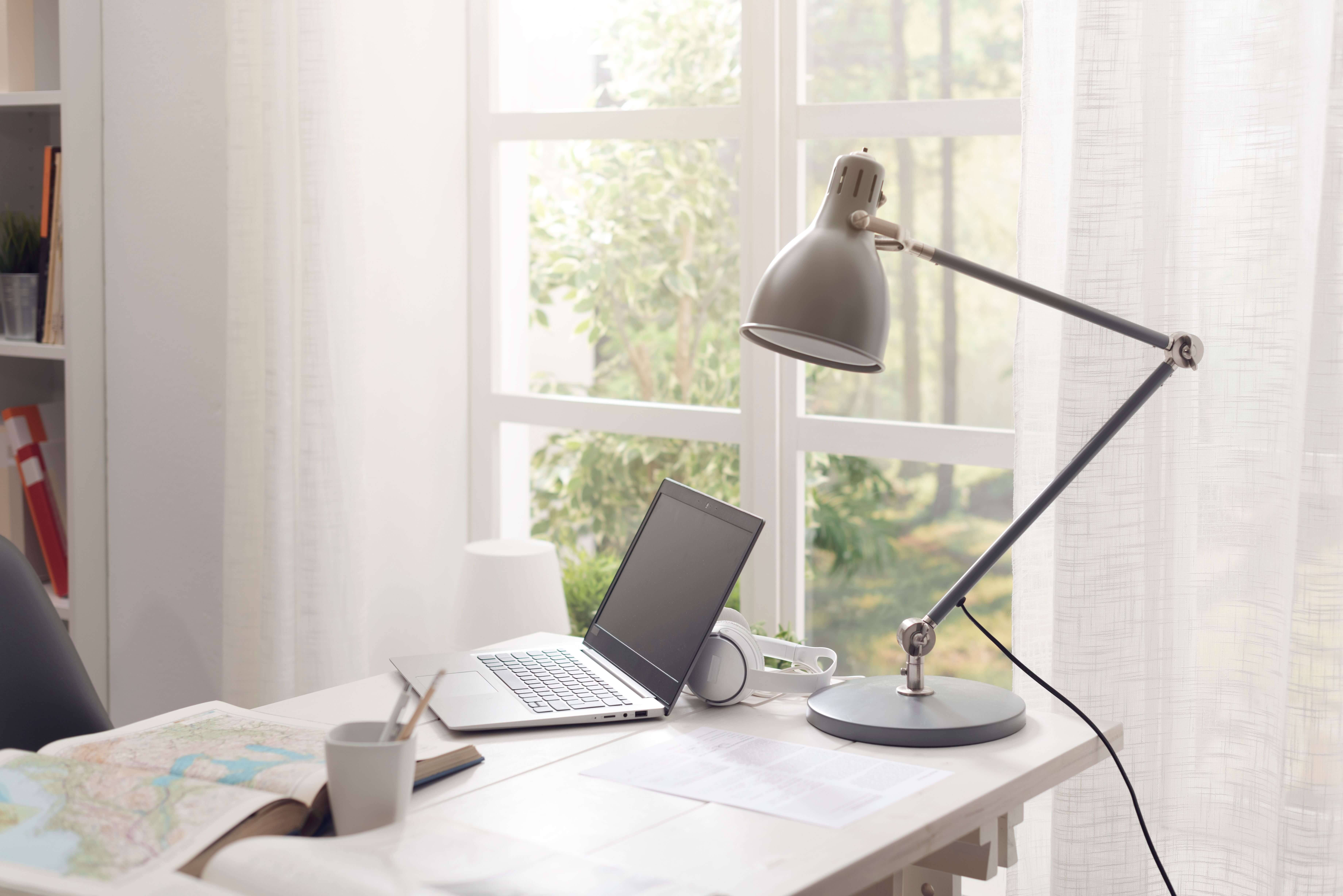 A table with a laptop, headset and a lamp with a white curtains